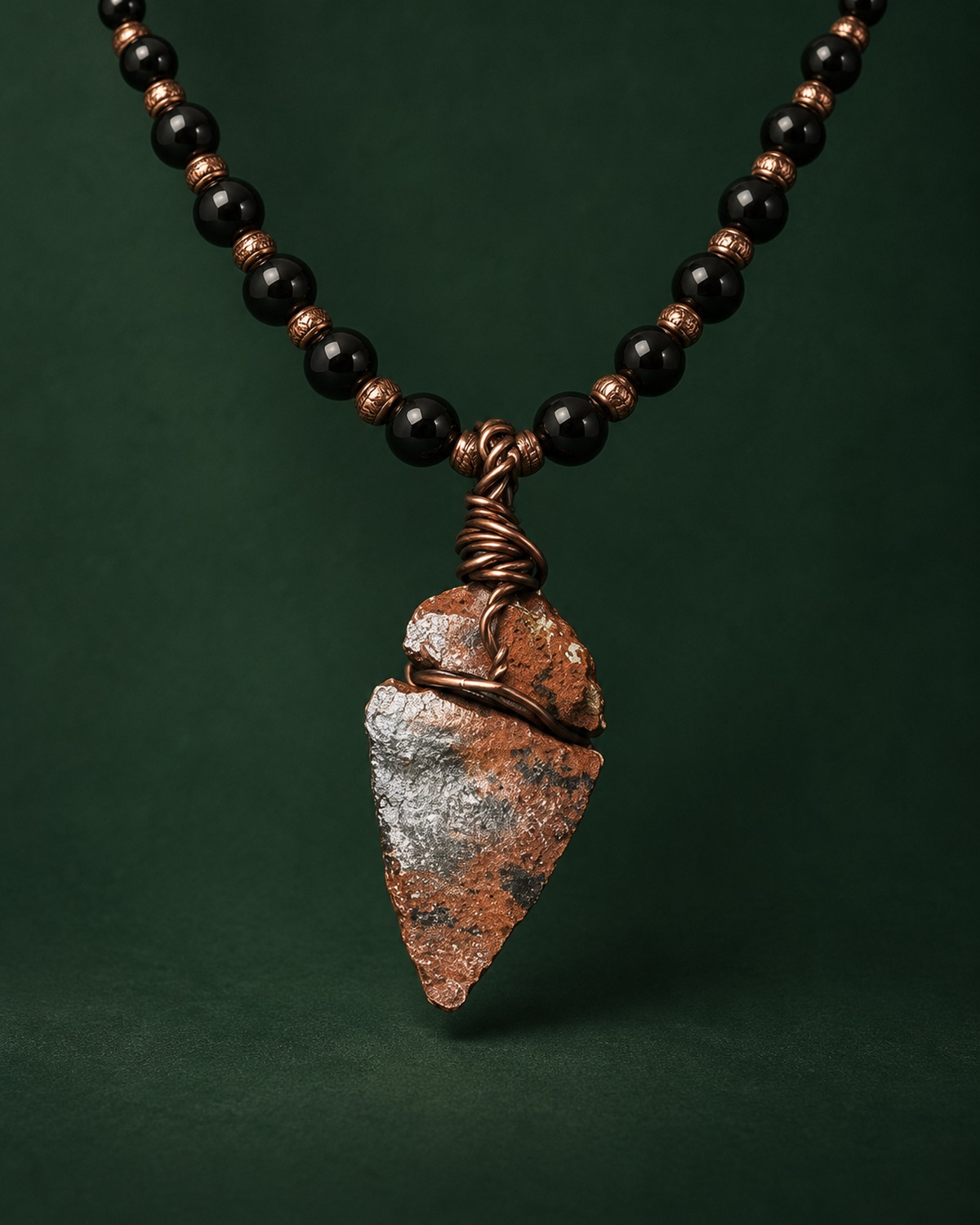 A mahogany obsidian pendant wrapped in copper wire, on a necklace of black beads with copper spacer beads.