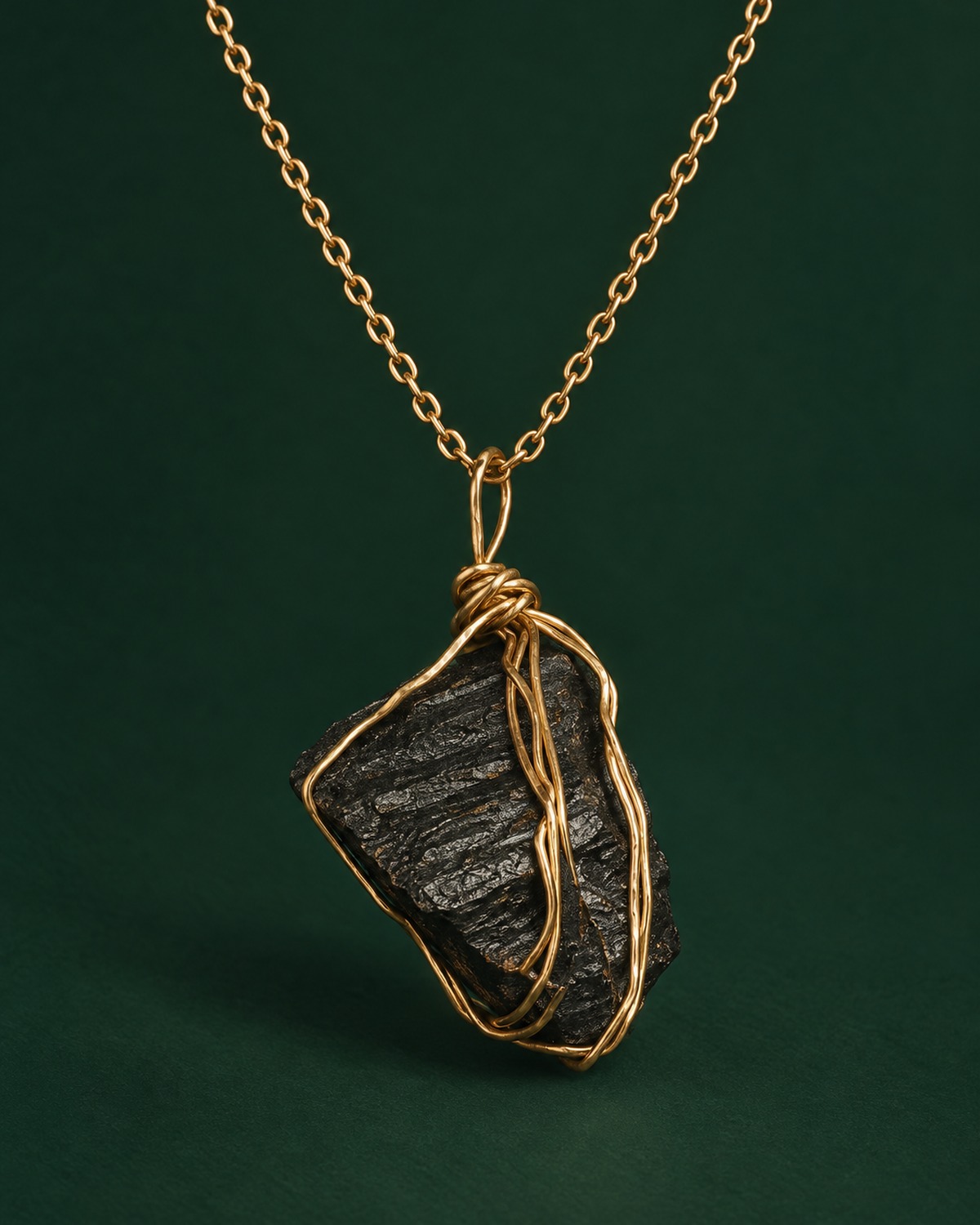 A raw black tourmaline stone wrapped in gold-tone wire, hanging from a fine gold chain.